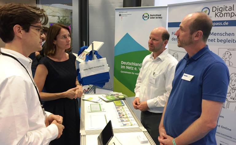 mehrere Personen unterhalten sich am Info-Stand des Digital-Kompass