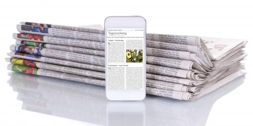 Smartphone mit Nachrichten-Website steht vor einem Stabel Zeitungen