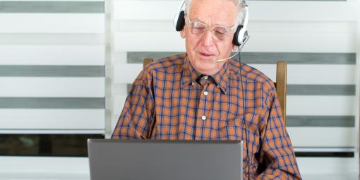 Älterer Herr arbeitet mit Headset am Laptop