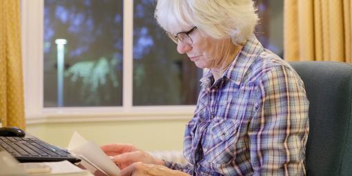 Ältere liest vor dem Laptop Rechnung