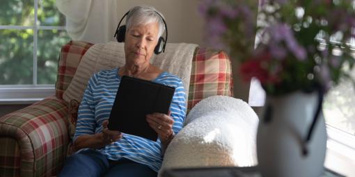 Frau sitzt im Sessel, liest am Tablet und hört Musik