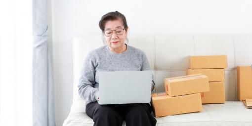 Ältere arbeitet am Laptop, neben ihr türmen sich Kartons