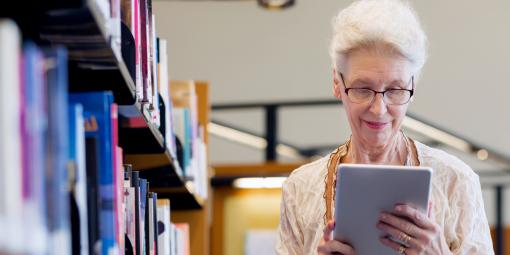 Frau steht neben einem Bücherregal und schaut auf ein Tablet