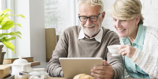 Beim Frühstück schaut ein älteres Paar mit Interesse auf einen Laptop.