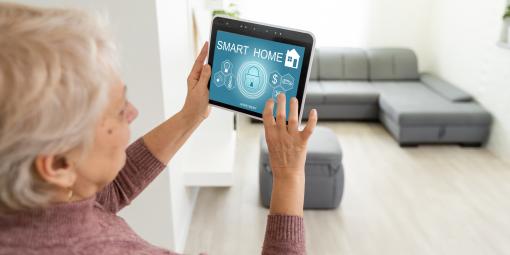 Ältere Dame, ein Tablet haltend, das Smart-Home-System steuernd