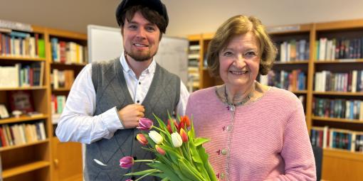 Zwei Personen (Frau C. mit Tulpen in der Hand und Bernd Josef Leisen). Beide stehen vor Bücherregalen in einem Raum im Albertinenhaus Hamburg. 
