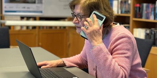 Frau C. sitzt vor einem Laptop und telefoniert gleichzeitig mit einem Handy in der Hand.