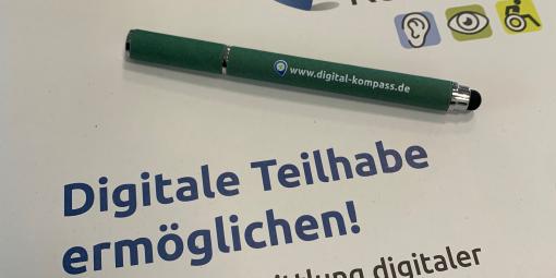 Eine Broschüre mit dem Titel "Digitale Teilhabe ermöglichen!" Ein Stift liegt darauf mit der Aufschrift: www.digital-kompass.de