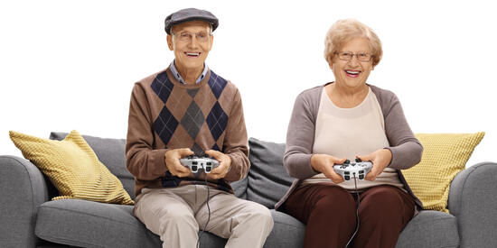 Frau und Mann sitzen lachend auf einem Sofa und spielen ein Videospiel