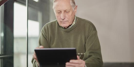 ein älterer Mann mit Tablet sitzt auf einer Treppe