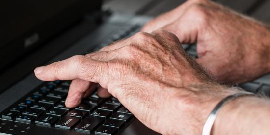 Eine ältere Person tippt auf einem Laptop.