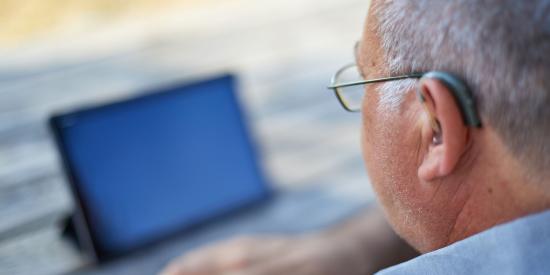 Selektiver Fokus eines älteren Mannes mit Hörgerät, der ein Tablet im Freien betrachtet