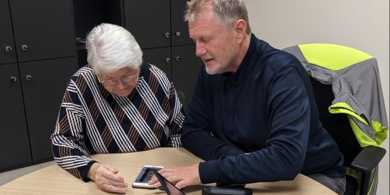 Ein Mann berät eine ältere Frau bei Anwendungen an ihrem Smartphone