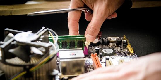 Zwei Hände die in einem offenen Computer etwas reparieren 