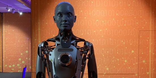 Ein menschenähnlicher Roboter vor einer orangen Wand.