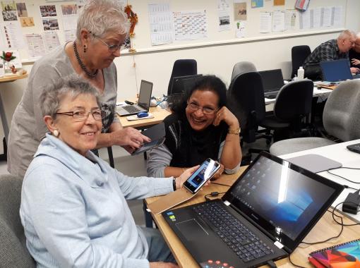 Drei Seniorinnen in einem Schulungsraum arbeiten gemeinsam am Laptop