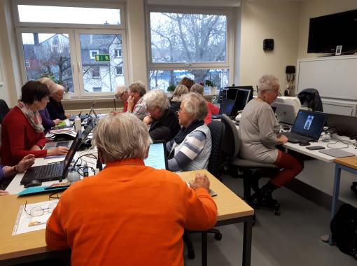 eine Gruppe Senioren arbeitet im Schulungsraum an Laptops