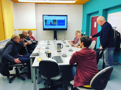 DigitalTreff Löbau Menschen sitzen am Tisch, im Hintergrund ein großer Wandbildschirm