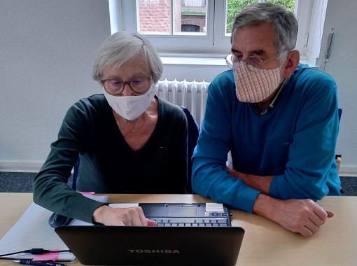 Mann und Frau sitzen mit Mundschutz am Laptop, Lernsituation unter Einhaltung aller aktuellen Hygienestandards