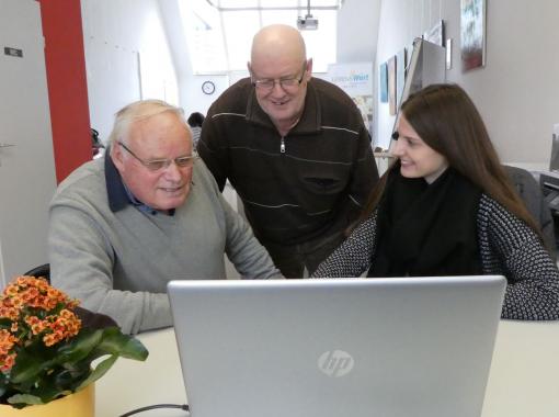 Junge Frau mit zwei älteren Herren vor Laptop
