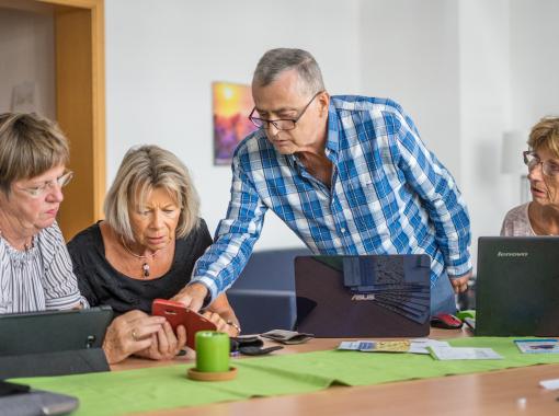 Lehrsituation am Tisch mit 4 Seniorinnen und Senioren,die am Laptop lernen