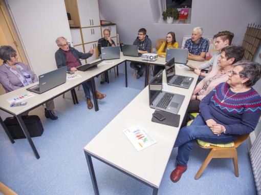 Eine Gruppe Senioren sitzt um einen Tisch herum und schaut auf Notebooks