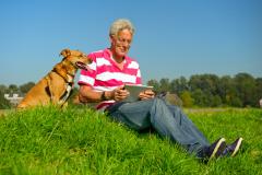 Älterer Herr auf einer Wiese mit Tablet und Hund