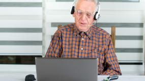 Älterer Herr arbeitet mit Headset am Laptop