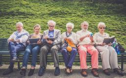 Sechs Personen mit verschiedenen Medien auf einer Bank