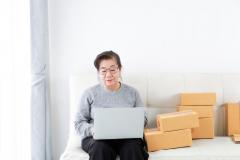 Ältere arbeitet am Laptop, neben ihr türmen sich Kartons