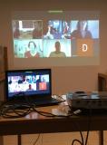 Eine Leinwand, auf der sechs Bildschirme einer Videokonferenz abgebildet sind