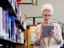 Frau steht neben einem Bücherregal und schaut auf ein Tablet