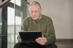 ein älterer Mann mit Tablet sitzt auf einer Treppe