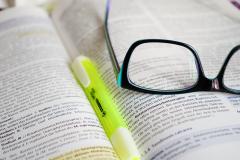 Textmarker und Brille liegen auf einem aufgeschlagenen Fachbuch