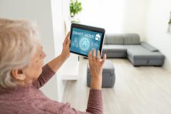 Ältere Dame, ein Tablet haltend, das Smart-Home-System steuernd