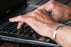 Eine ältere Person tippt auf einem Laptop.