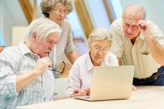 Eine Gruppe Senior:innen betrachtet einen Laptop.