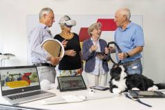 vier Senior:innen halten unterschiedliche Geräte in den Händen, die Künstliche Intelligenz beinhalten
