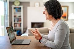 Ältere Dame sitzt am Tisch und hat eine Videokonferenz mit einer jüngeren Person.