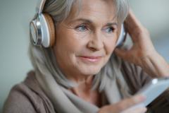 Eine ältere Frau mit Kopfhörern und Handy.
