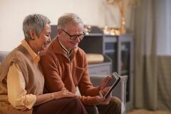 Ein älteres Paar sitzt auf dem Sofa und schaut gemeinsam auf ein Tablet.