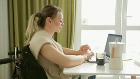 Eine junge Frau sitzt am Tisch in einem Rollstuhl. Sie nutzt einen Laptop. 