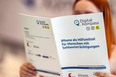 Eine junge Frau liest den Leitfaden des Digital-Kompass "iPhone als Hilfsmittel für Menschen mit Sehbeeinträchtigung".
