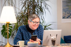 Eine Frau sitzt vor dem Laptop und hat ein Smartphone in der Hand.