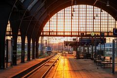 Das Bild zeigt einen Bahnhof mit einfahrendem Zug bei Sonnenaufgang