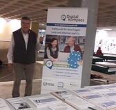 Siegbert Schlor steht neben dem Aufsteller des Digital-Kompass. Darauf steht "www.digital-kompass.de - Treffpunkt für Ihre Fragen rund ums Internet und Co."