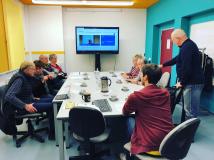 DigitalTreff Löbau Menschen sitzen am Tisch, im Hintergrund ein großer Wandbildschirm