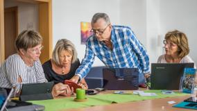 Lehrsituation am Tisch mit 4 Seniorinnen und Senioren,die am Laptop lernen