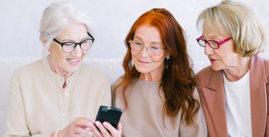 Drei ältere Damen nutzen ein Smartphone und lächeln dabei.