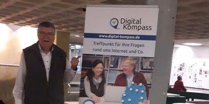 Siegbert Schlor steht neben einem Digital-Kompass Aufsteller und zeigt darauf.